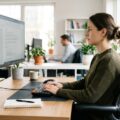Person sidder korrekt ved arbejdsbord med monitor i øjehøjde for optimal ergonomi